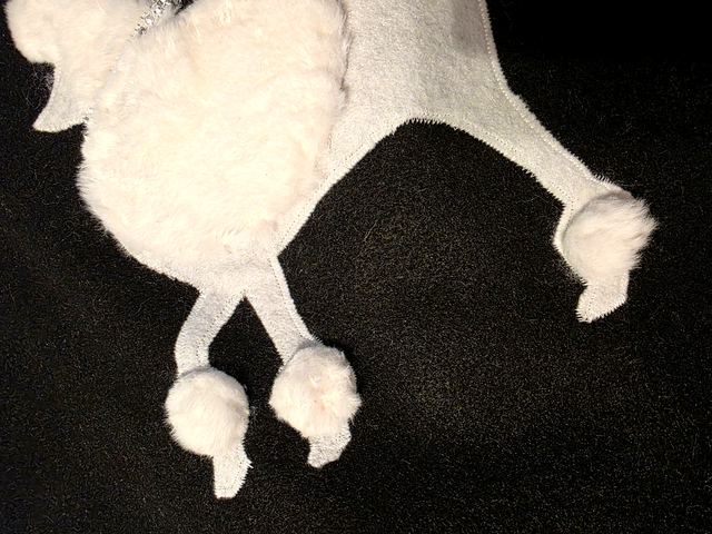 Close-up of the white poodle applique on black fabric, with fluffy pom-pom feet