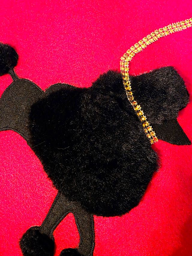 The black poodle's head with a gold leash on hot pink fabric